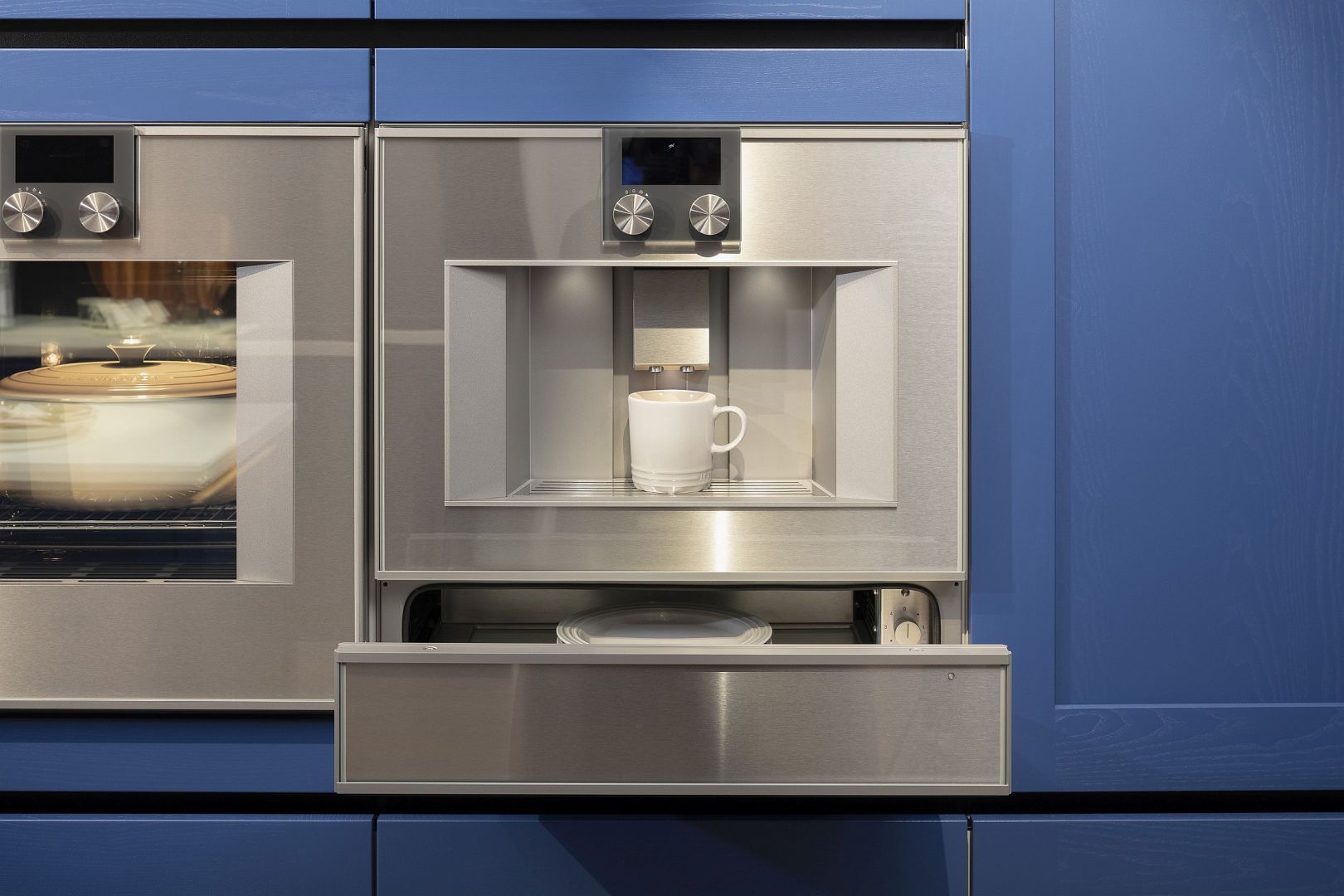 Einbaukaffeevollautomat mit geöffneter Wärmeschublade darunter in saphierblauer Häcker-Küche
